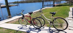 Bicycles parked on a lake's edge, surrounded by a grassy area and stone pathway.