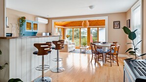 A spacious kitchen with a wooden ceiling, a dining area with a table and chairs, and a large window offering a view of the outdoors. - The sunroom on Maple  (Picton)