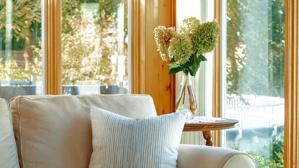 A cozy room with a beige sofa, a small round table, and a vase with flowers. - The sunroom on Maple  (Picton)