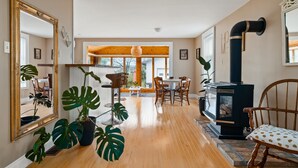 A spacious living room with a large mirror, wooden flooring, and a black wood stove. - The sunroom on Maple  (Picton)