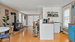 A modern kitchen with white cabinetry, a central island, and a dining area with wooden chairs and a table. - The sunroom on Maple  (Picton)