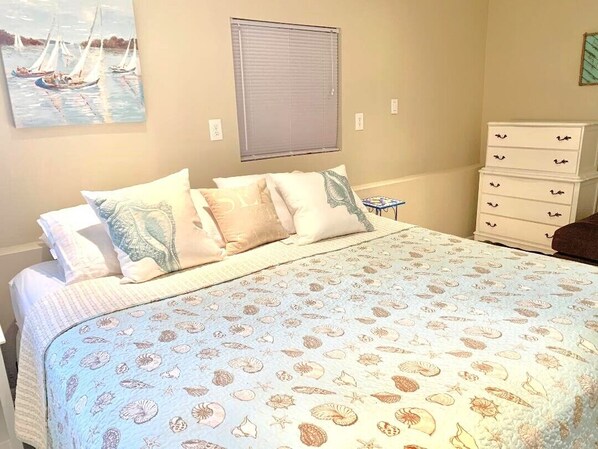 A bedroom with a bed, a window, a dresser, and a painting on the wall.