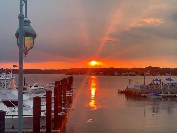 A marina with boats docked, a sunset in the background, and a street lamp in the foreground.