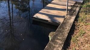 Une jetée en bois s’étendant au-dessus d’une rivière paisible, entourée d’arbres et de verdure.