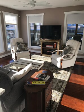 Un salon comprenant un canapé, deux fauteuils, une table basse, un téléviseur posé sur un meuble en bois, et une vue dégagée grâce à de grandes fenêtres.