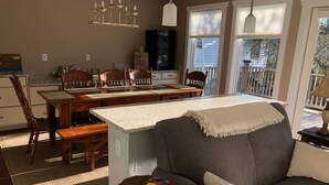 Un salon chaleureux comprenant un coin repas, un canapé gris et une petite table sur laquelle sont posés des livres et un smartphone.