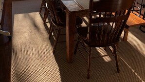 Un coin repas avec une grande table en bois, six chaises et une vue sur une terrasse, visible à travers de grandes fenêtres.