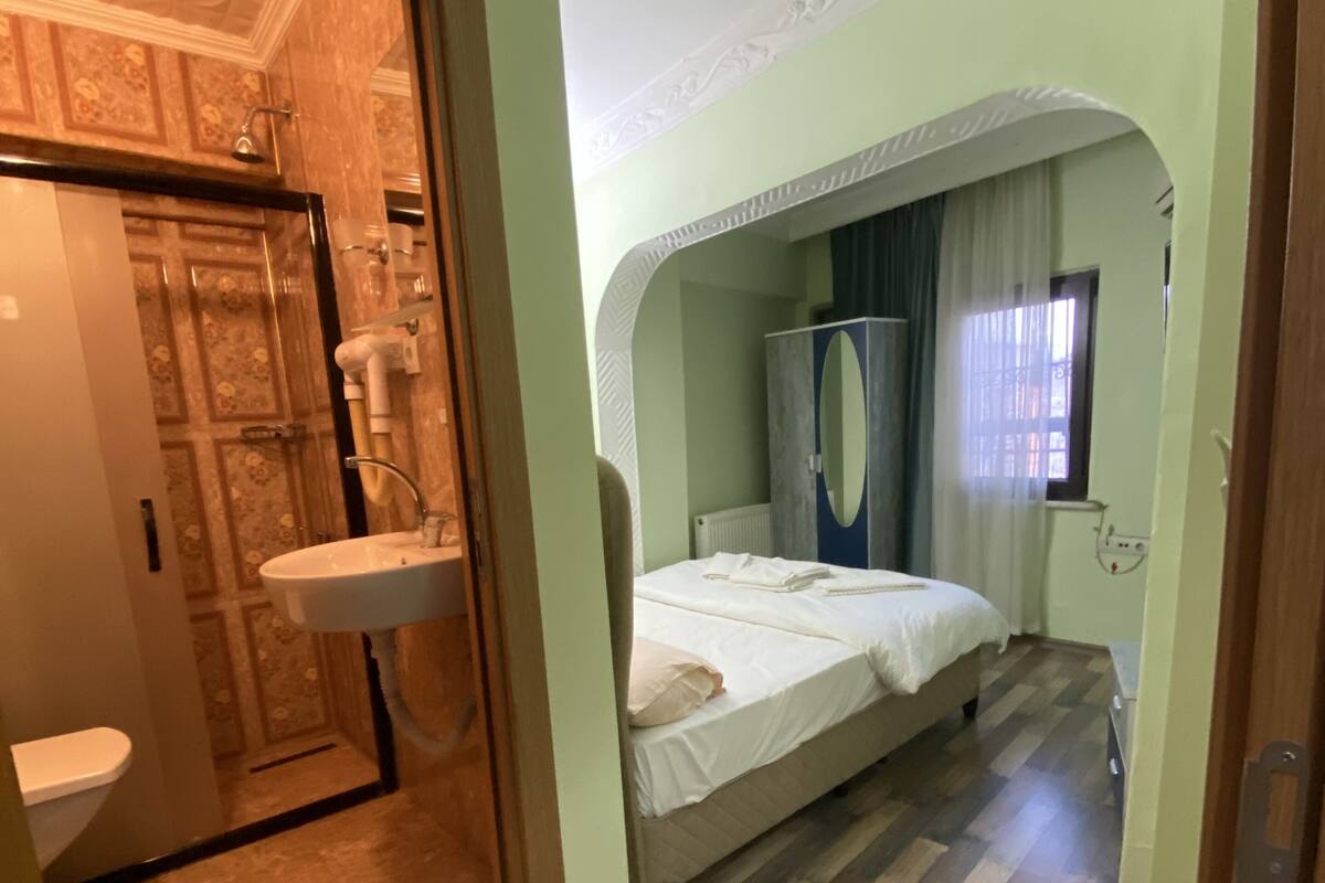 A room with a bunk bed, a small window with blinds, a mirror, and a wooden floor.