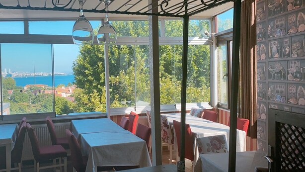 A restaurant with large windows offering a view of a city skyline and a body of water. Tables are arranged for dining. - Redamancy Hotel (Istanbul)