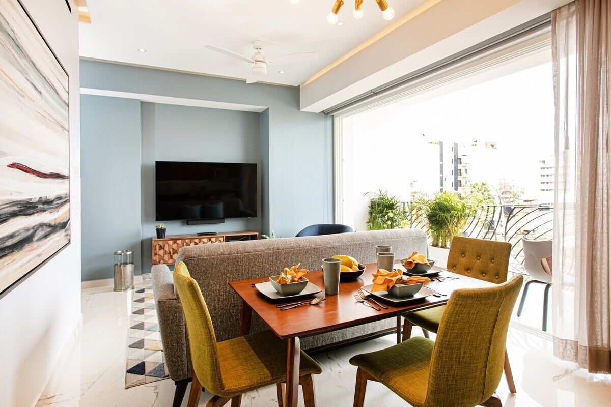 A modern living room with a dining area, a flat-screen TV, and a balcony with plants.