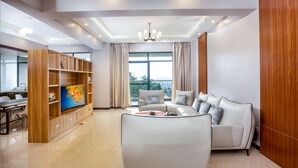 Una sala de estar moderna con un sofá blanco, un televisor sobre un mueble de madera y un comedor con sillas.