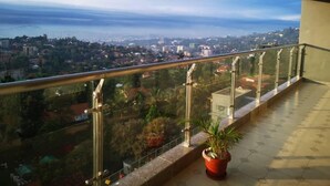 Un balcón con barandilla de vidrio que ofrece vistas a un paisaje urbano con edificios y una masa de agua distante.