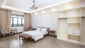 Un dormitorio moderno con una cama grande, dos mesitas de noche, un banco, un armario y vistas de la ciudad a través de una ventana.