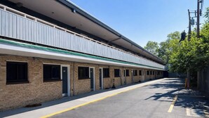 Un motel de una sola planta y larga hilera de habitaciones, con un corredor cubierto y un estacionamiento.