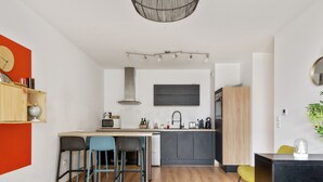 A modern kitchen with a central island, bar stools, a built-in oven, and a microwave. - Appartement Corselle - Welkeys (Mouvaux)