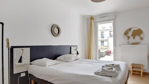 A neatly made bed with white linens, a bedside lamp, and a small stool. - Appartement Corselle - Welkeys (Mouvaux)