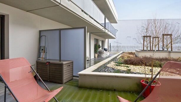 A balcony with two red chairs, a storage unit, and a small garden area with plants and pebbles. - Appartement Corselle - Welkeys (Mouvaux)