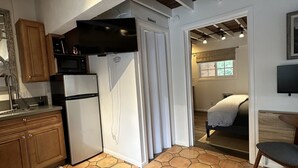 A compact kitchen with a microwave, refrigerator, and wooden cabinets. A dining area with a chair and ottoman is visible. - El Bungaló Privado (San Clemente)