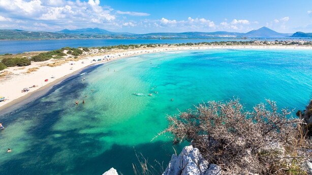Una playa costera con aguas turquesas cristalinas, orillas de arena y un telón de fondo montañoso.