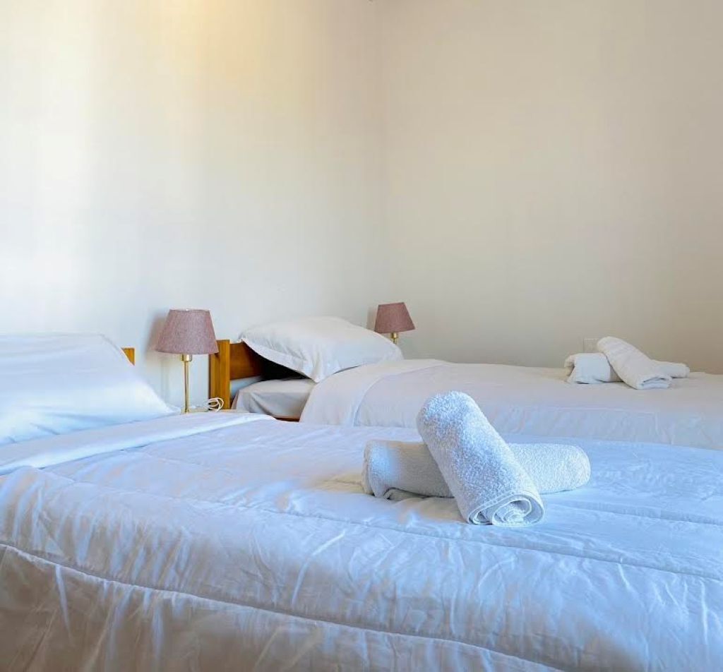 A hotel room with two beds, each with white linens and pillows, and two bedside lamps.