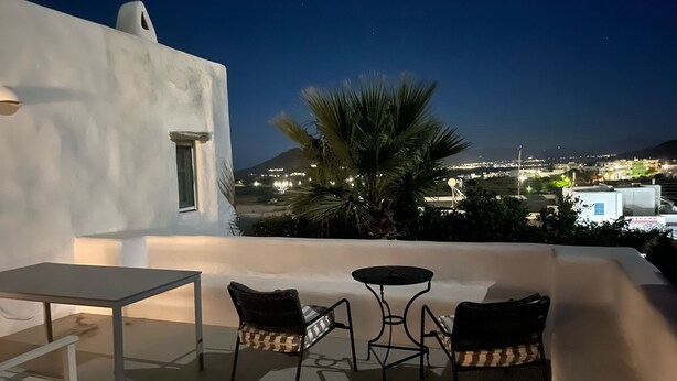 Eine Terrasse mit Tisch und Stühlen mit Blick auf eine nächtliche Stadtlandschaft.