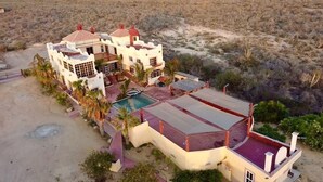 A large, two-story house with a swimming pool, surrounded by desert vegetation.
