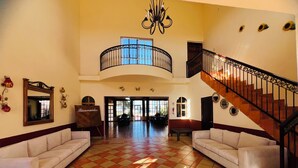 A spacious lobby with a high ceiling, a central staircase, and a large window allowing natural light.