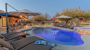 Ein Pool mit Liegestühlen und Sonnenschirmen, umgeben von einer Terrasse mit Lichterketten.