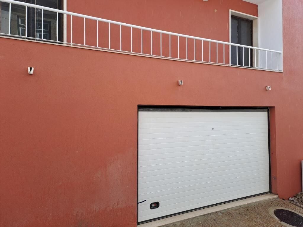 Un edificio con fachada roja, una puerta de garaje blanca y un balcón con barandilla blanca.