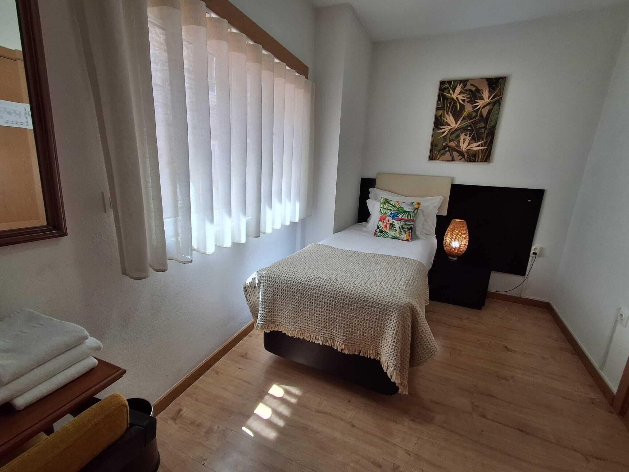 Une chambre à coucher avec un lit, une table de chevet, une lampe et une fenêtre avec des rideaux.
