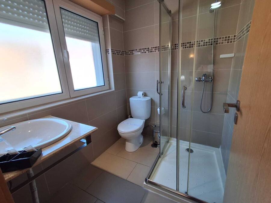 A bathroom with a glass-enclosed shower, a toilet, and a sink.