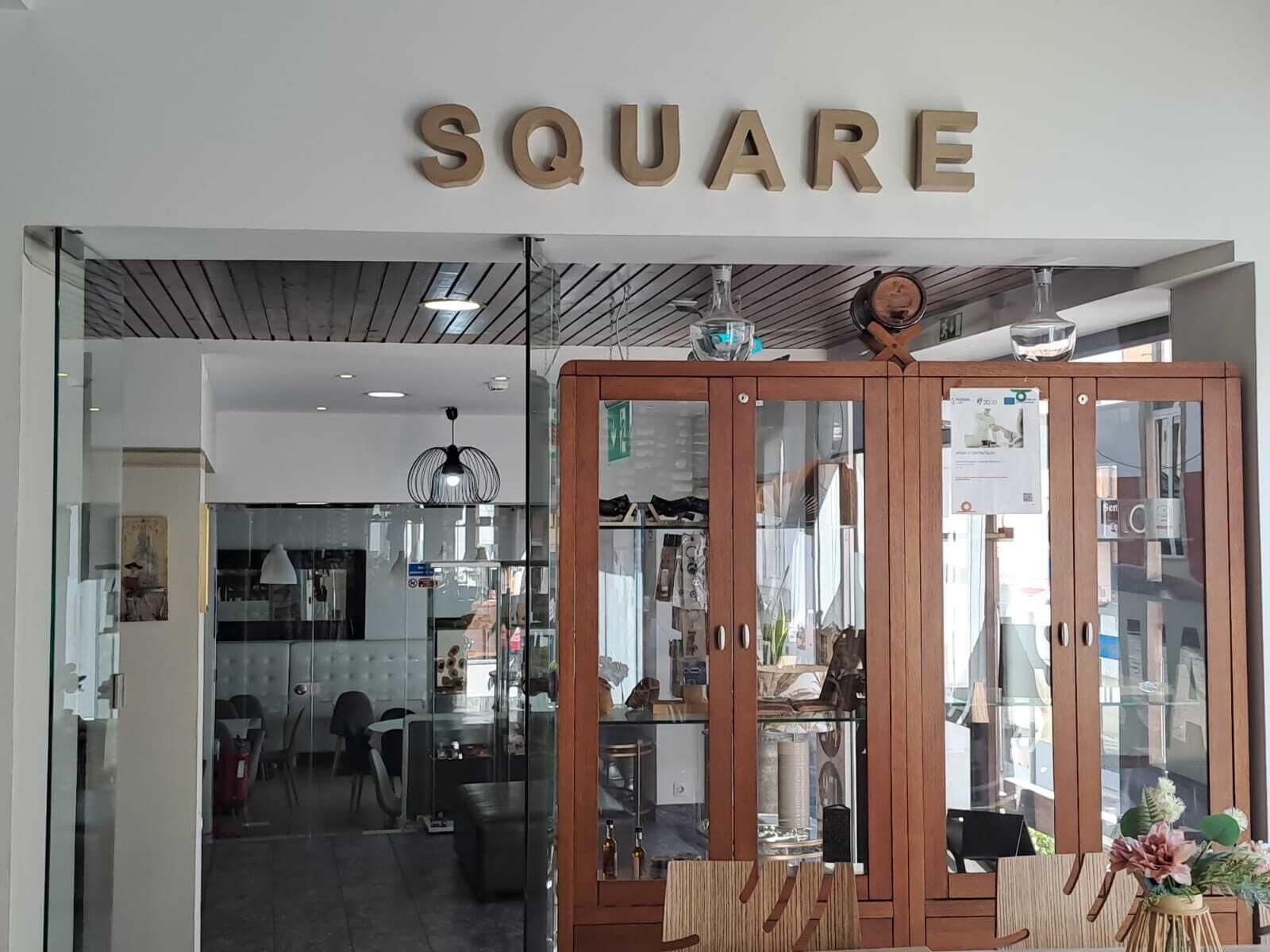 A storefront with a sign reading 'SQUARE' and a wooden cabinet with glass doors displaying various items.