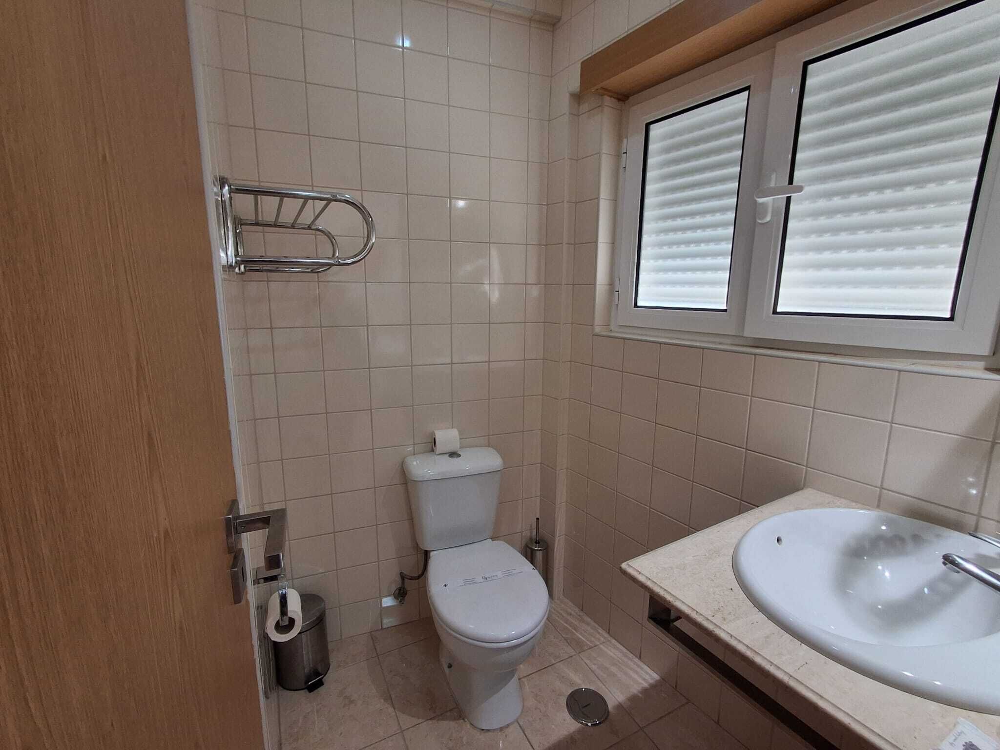 A bathroom with a toilet, sink, and window with blinds.