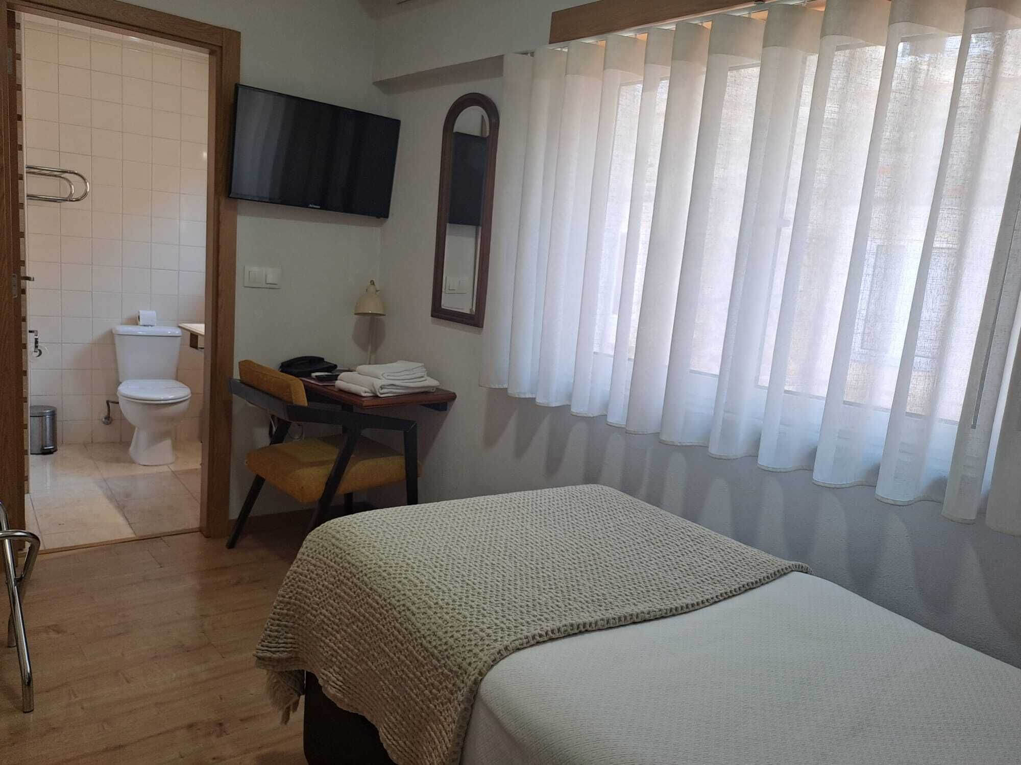 Een slaapkamer met een bed, een bureau, een stoel, een toilet en een douche.