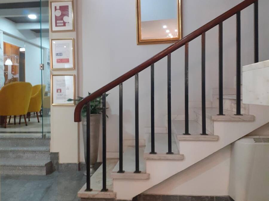 Eine Treppe mit hölzernem Geländer und schwarzen Spindeln, die zu einer Zwischenebene mit einem gerahmten Spiegel und Zertifikaten an der Wand führt.