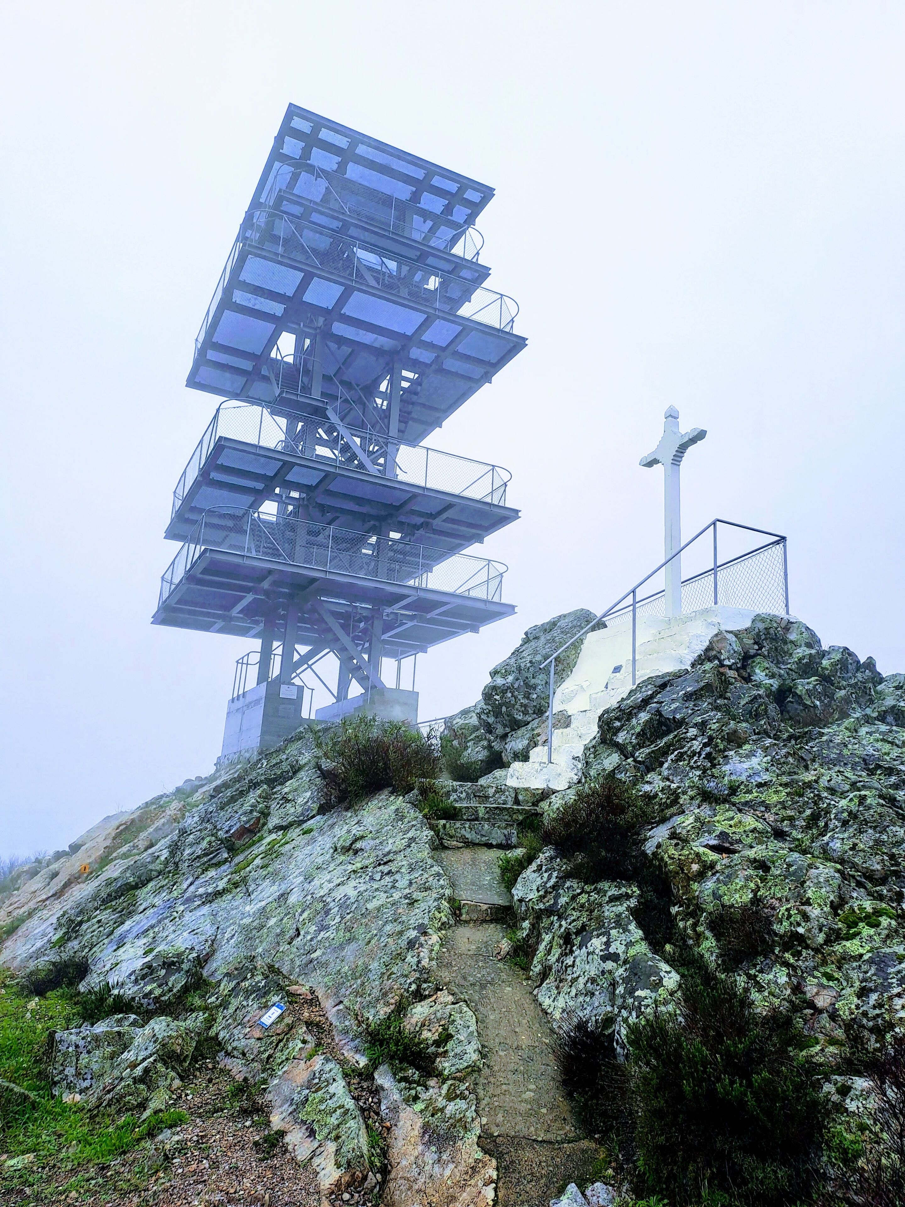 A multi-tiered observation tower with a staircase leading to the top, surrounded by rocky terrain and vegetation.