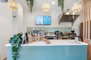 Interno di una caffetteria moderna con un bancone, luci a sospensione, una lavagna per il menù e attrezzature da cucina.