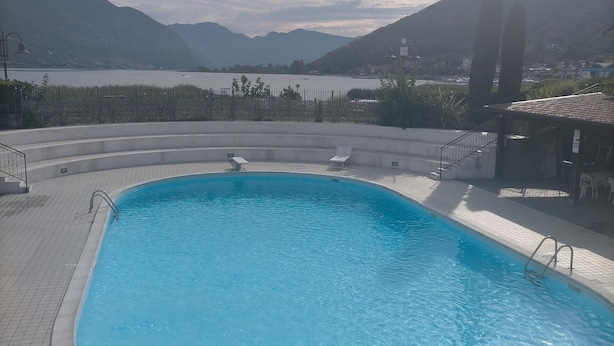 En swimmingpool med fliseterrasse, en solbelyst himmel og bjerge i baggrunden.