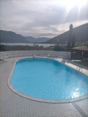 Uma piscina com deck revestido de azulejos, céu ensolarado e montanhas ao fundo.