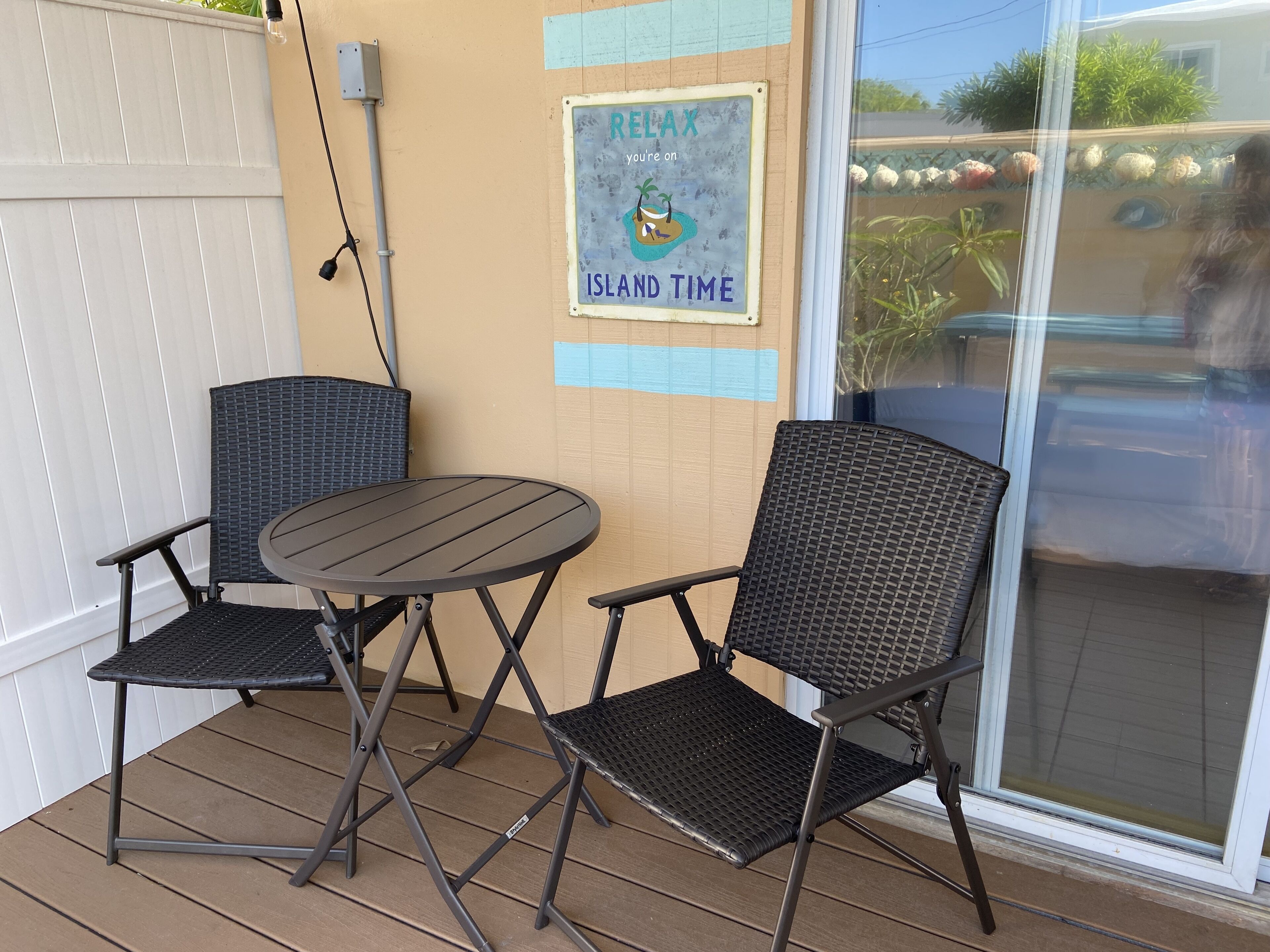 A patio area with two chairs and a table, a sign that reads 'RELAX your island time,' and a view of the outside through a glass door.