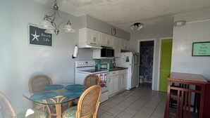 Une cuisine compacte avec des meubles blancs, une table à manger entourée de chaises en osier et une petite table en bois.