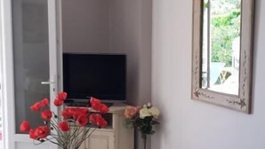 Una sala de estar con televisor, un jarrón con flores rojas, un espejo y un sofá.