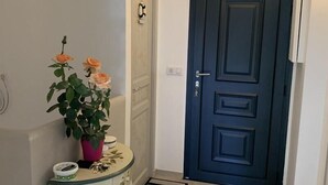 Un pasillo con una puerta azul oscuro, una mesita con una planta en maceta y una pared blanca.