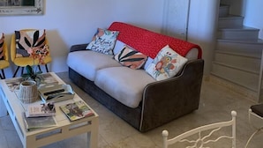 Una sala de estar con sofá, mesa de centro con revistas, candelabro, espejo y escalera.