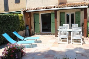 An outdoor patio with a table and chairs, a pool, and a covered area with a door and shutters. - Joli Gîte les Palmiers III (LA CROIX VALMER)
