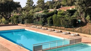 Una piscina rectangular con solárium alicatado, rodeada de sillas de descanso y una barandilla metálica.