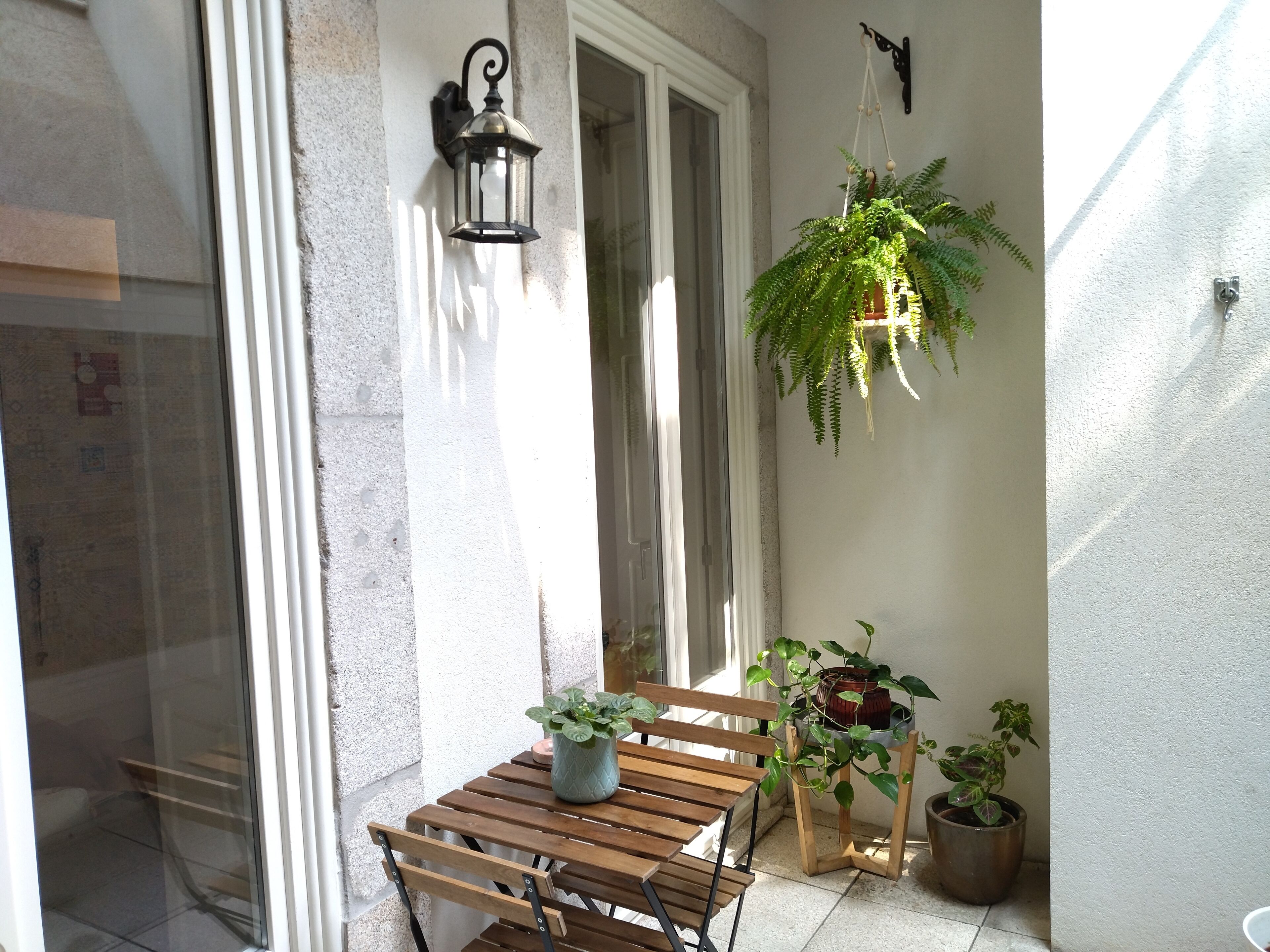 A wooden bench with a potted plant, a hanging lantern, and two potted plants against a wall.