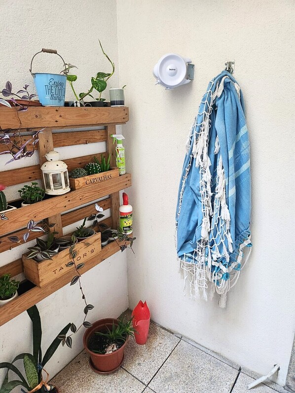 A corner with a wooden plant shelf, a hanging blue towel, and a white wall-mounted light fixture.