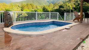 Une piscine agrémentée d’une cascade, entourée d’une terrasse en bois et d’une balustrade blanche.
