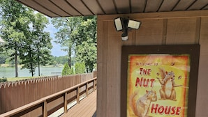 Eine Holzterrasse mit Blick auf einen See und Bäume, und ein Schild mit der Aufschrift 'Welcome to The Nut House'.